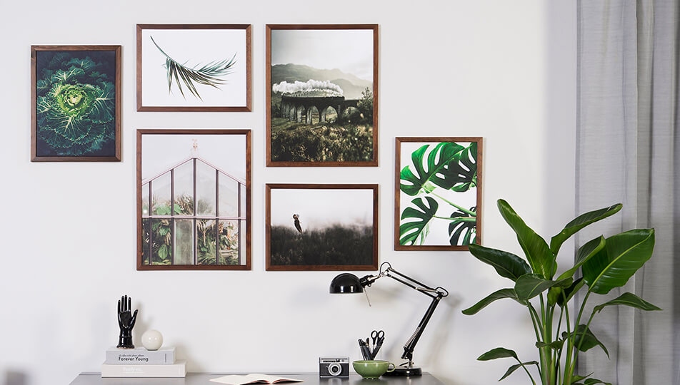 Bilderwand im Büro - dunkle Holzrahmen und grüne Naturmotive